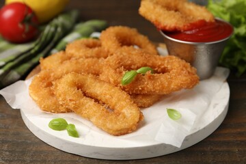 Deep fried squid rings with basil and ketchup on wooden table, closeup