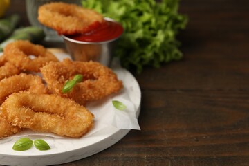 Deep fried squid rings with basil and ketchup on wooden table, closeup. Space for text