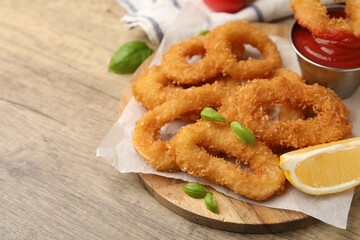 Deep fried squid rings with lemon slice, basil and ketchup on wooden table, closeup. Space for text