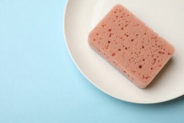 Kitchen sponge and plate on light blue background, top view. Space for text