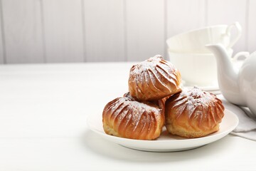 Tasty profiteroles with powdered sugar served on white wooden table. Space for text