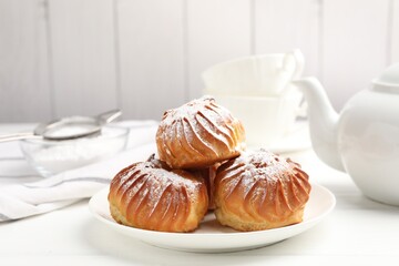 Tasty profiteroles with powdered sugar served on white wooden table, closeup