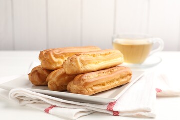 Tasty eclairs and tea on white wooden table, closeup