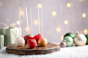 Tasty cake pops with sprinkles on artificial snow against grey background with blurred lights, closeup with space for text. Christmas snack