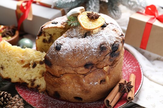 Tasty Christmas panettone cake with powdered sugar and festive decor on table, closeup