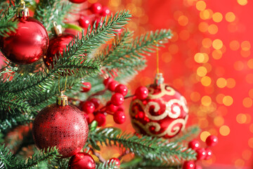 Naklejka premium Beautiful ornaments on Christmas tree against red background with blurred lights, closeup. Bokeh effect