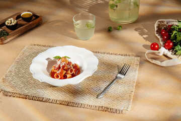 Elegant plate of pasta with tomato sauce and parmesan on a woven placemat under warm sunlight. Fresh tomatoes, herbs and lemonade create a cozy Mediterranean dining atmosphere.