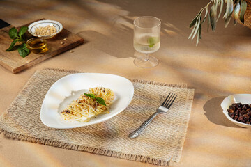 Plate of spaghetti with basil and grated cheese on a rustic table setting under warm Mediterranean sunlight. Wine glass, olives, and pine nuts create an elegant Italian dining mood.
