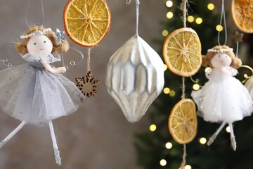 Beautiful fairy doll and dried orange slices hanging on string against blurred lights, closeup. Christmas decor