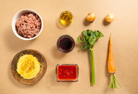 Colorful ingredients are laid out on a kitchen counter, including ground meat, tomatoes, pasta, and fresh vegetables. These items are ready for a delicious homemade meal. - Powered by Adobe