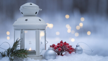 Christmas lantern with candle on snow in winter forest. Bokeh background with garland lights, silver balls