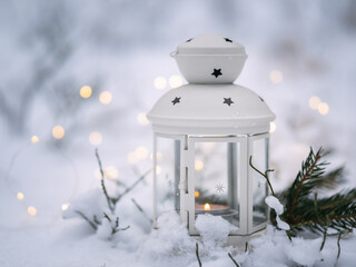 candle lantern stands in the snow in a forest. Christmas background with garland lights and copy space.