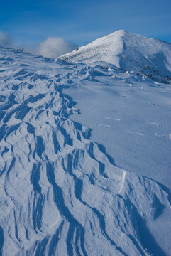 View of a pristine white landscape, sculpted by wind into delicate snow waves, leading to a majestic snow-capped peak under a clear blue sky, in Babky, Western Tatras, Jamnik, Zilinsky kraj, Slovakia.