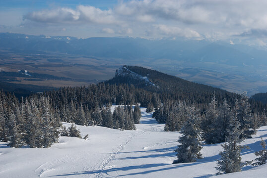 View of snow-covered trees and hills under a blue sky with white clouds, creating a winter wonderland over Mnich, Jamnik, Zilinsky kraj, Slovakia.