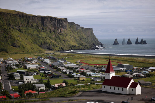 Picturesque icelandic coastal village nestled beneath dramatic green cliffs with sea stacks in the distance