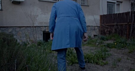 An elderly man in a blue coat meticulously tends to his home garden, observing and nurturing the growing plants. This scene captures a peaceful, active lifestyle and connection with nature.