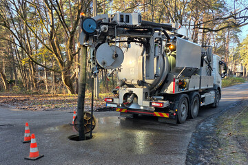 Hydro-vac sewer cleaning truck servicing underground pipeline through open manhole on a forest road
