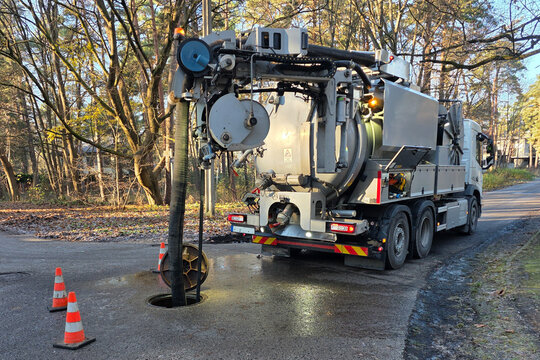 Hydro-vac sewer cleaning truck servicing underground pipeline through open manhole on a forest road