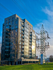 Modern apartment building with high-voltage transmission tower and power lines on a sunny day