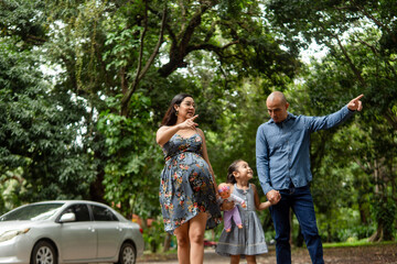 Fototapeta premium Pregnant mother, father, and daughter pointing directions in park