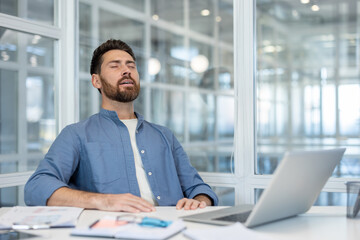 Businessman relaxing and performing breathing exercises at his office desk, finding mental peace and stress relief during a busy workday by taking a quiet moment