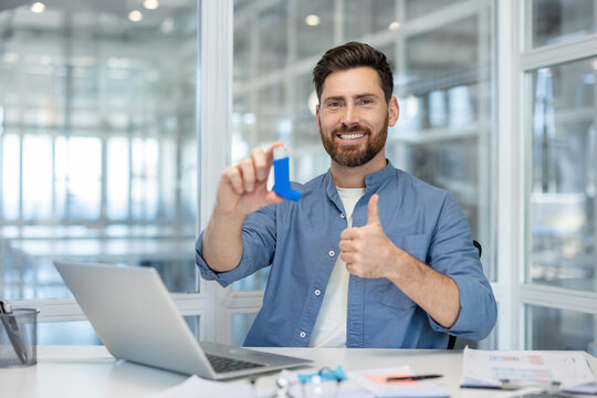 Smiling man finding relief and successful treatment for his respiratory condition, holding an asthma inhaler and giving a confident thumbs up in a bright office environment