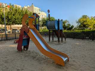 Colorful modern children's playground with slide and sand by beach of Platja de Palma, El Arenal, Mallorca. Tourist, recreation, residential area, apartment buildings, hotels, Mediterranean resort.