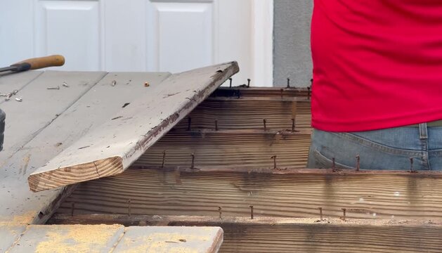Workman prying old boards off of supporting joists