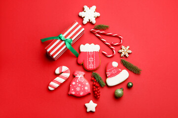Tasty gingerbread cookies, gift and Christmas decor on red background, flat lay