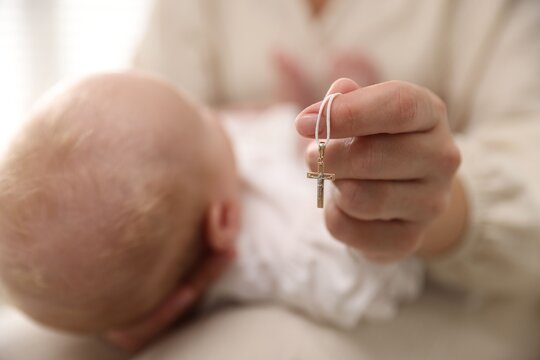 Sacrament of baptism. Woman holding little baby and gold cross indoors, selective focus - Powered by Adobe