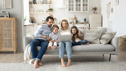 Happy family parents with kids gather on sofa using notebook