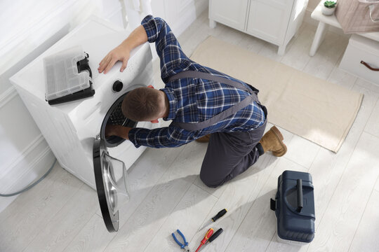 Repairman fixing broken washing machine at home, above view