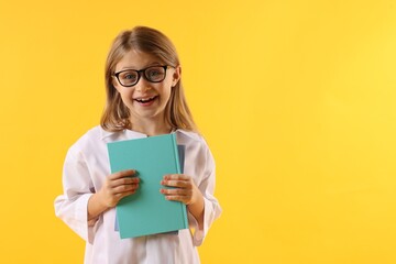Smiling little girl in laboratory coat and glasses with book on yellow background, space for text. Child and science