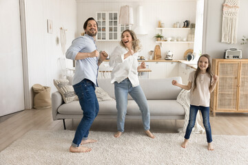 Overjoyed parents with little daughter jump dance in bright apartment