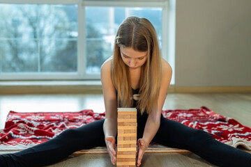 Girl concentrating on tall wooden block tower. A teenage girl sits on the floor with a festive blanket, carefully aligning a tall stack of wooden blocks in a quiet room.