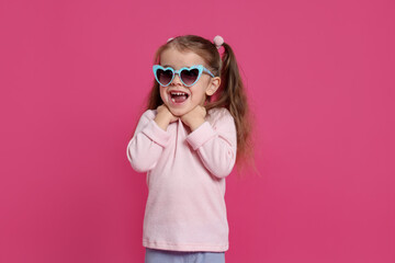 Emotional little girl in sunglasses on pink background