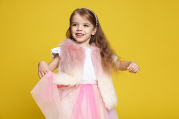 Happy little girl in fur vest and skirt on yellowish green background