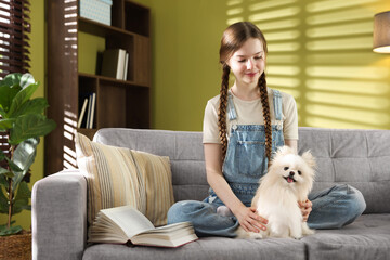 Teenage girl with Pomeranian dog on sofa at home