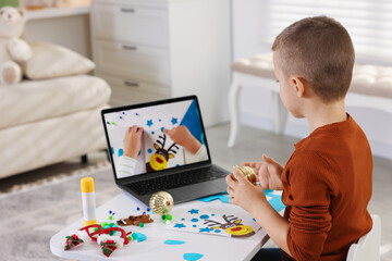 Little boy making Christmas postcard by video tutorial at table indoors. Child handmade craft