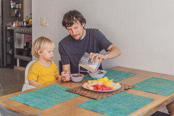 A father having breakfast at the table with his young son in a bright home kitchen, sharing a warm morning moment. Family bonding, parenting, everyday routine and healthy lifestyle concept
