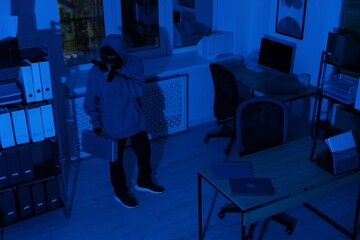 Thief with gun and briefcase in office at night