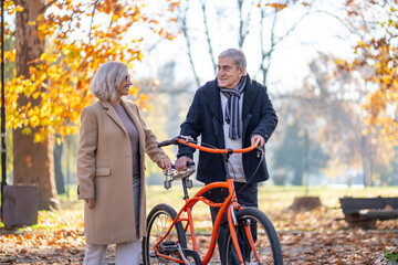 Happy senior couple enjoying a walk in the park with a bicycle on a sunny autumn day