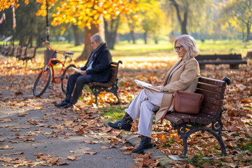 Couple enjoying a relaxing autumn day in the park, reading books on a bench