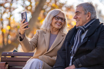 Happy senior couple taking a selfie together in a park during autumn