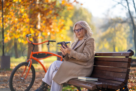 Senior woman using smartphone in autumn park with bicycle