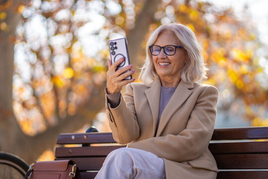 Smiling senior woman video calling on smartphone in a park during autumn