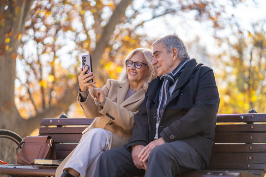 Happy senior couple taking a selfie together in a park on a sunny autumn day