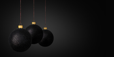 Three black glitter Christmas baubles hanging on thin strings against a dark background, creating a...