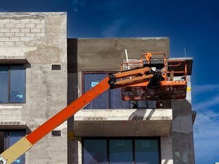 Worker using an articulated boom lift beside a building exterior under construction