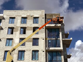 Worker using an articulated boom lift beside a building exterior under construction
